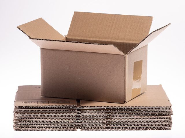 An open corrugated carton standing on a stack of flat-packed boards