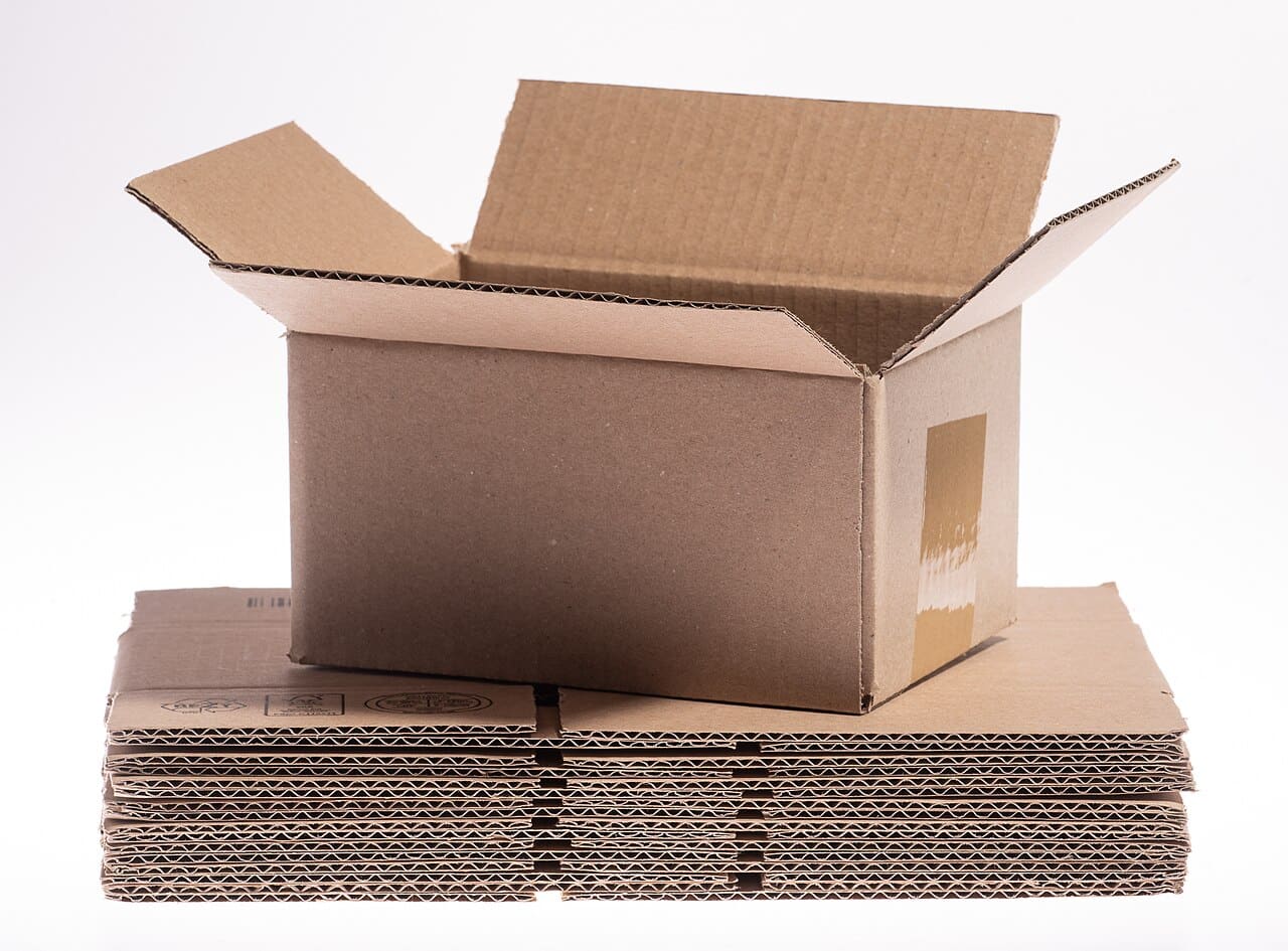 An open corrugated carton standing on a stack of flat-packed boards
