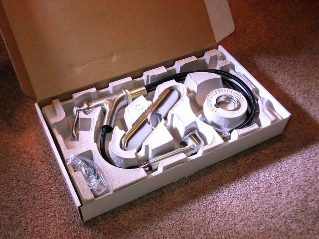 A tap and its fittings held in a grey moulded pulp insert inside its box