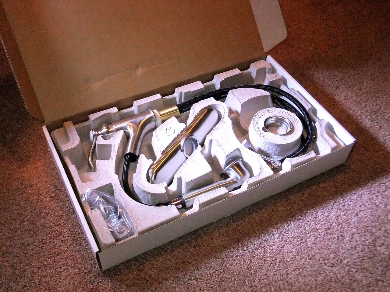 A tap and its fittings held in a grey moulded pulp insert inside its box