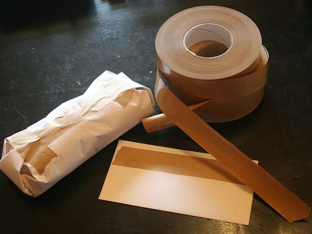 Rolls of brown gummed paper tape beside a strip and a paper-wrapped parcel