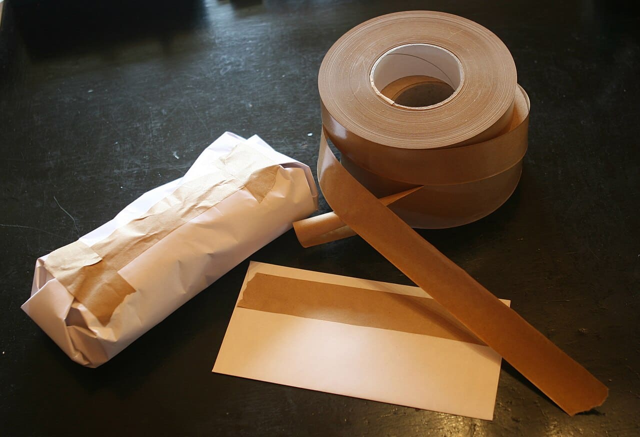 Rolls of brown gummed paper tape beside a strip and a paper-wrapped parcel