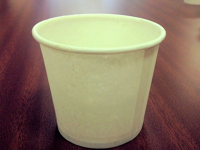 A plain unprinted paper cup on a dark wooden table