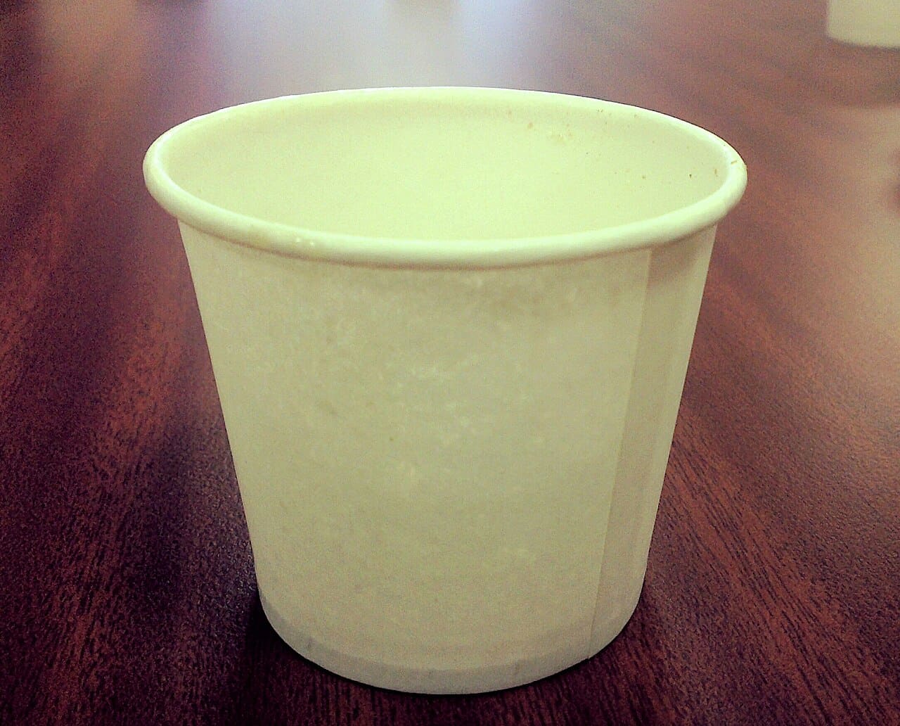 A plain unprinted paper cup on a dark wooden table