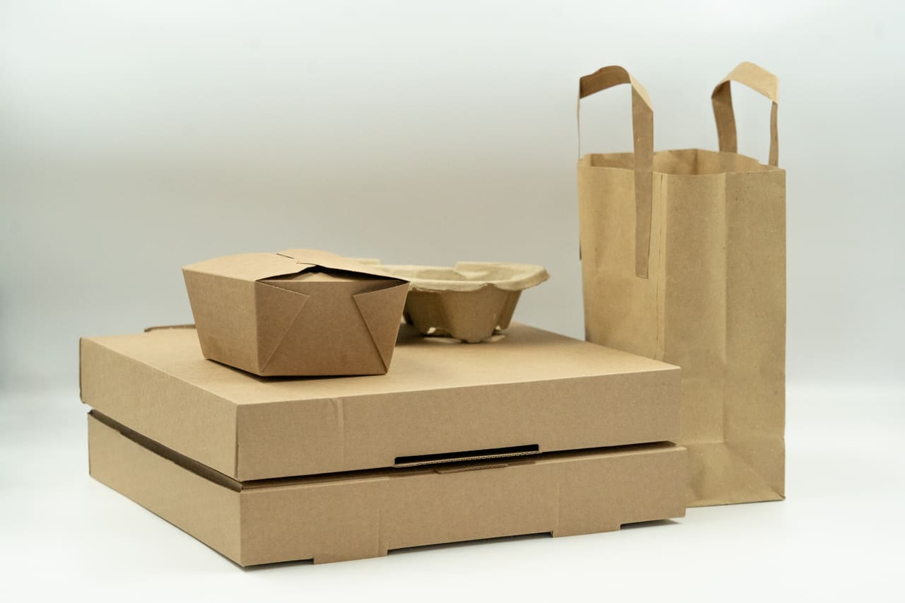 Brown board boxes, a food box and a paper carrier bag on a pale background