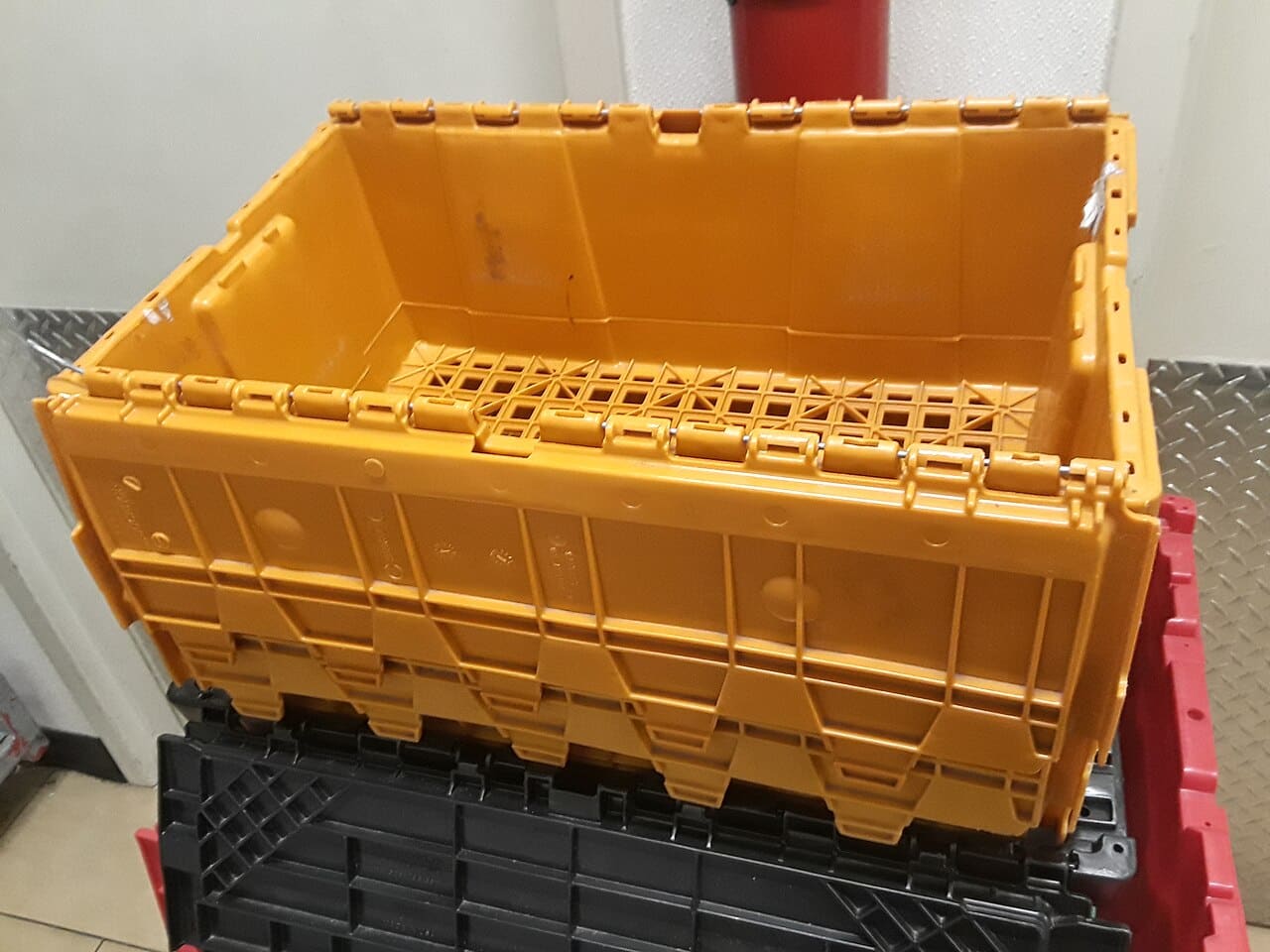 A stackable plastic tote with hinged lid flaps, on top of other crates